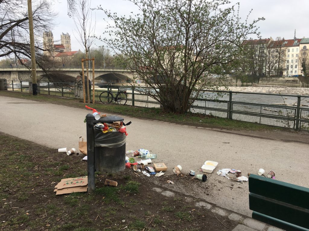 Überquellender Mülleimer mit Pappbechern mit Deckel und weiteren Einweg-Verpackungen drumherum an der Isar in München
